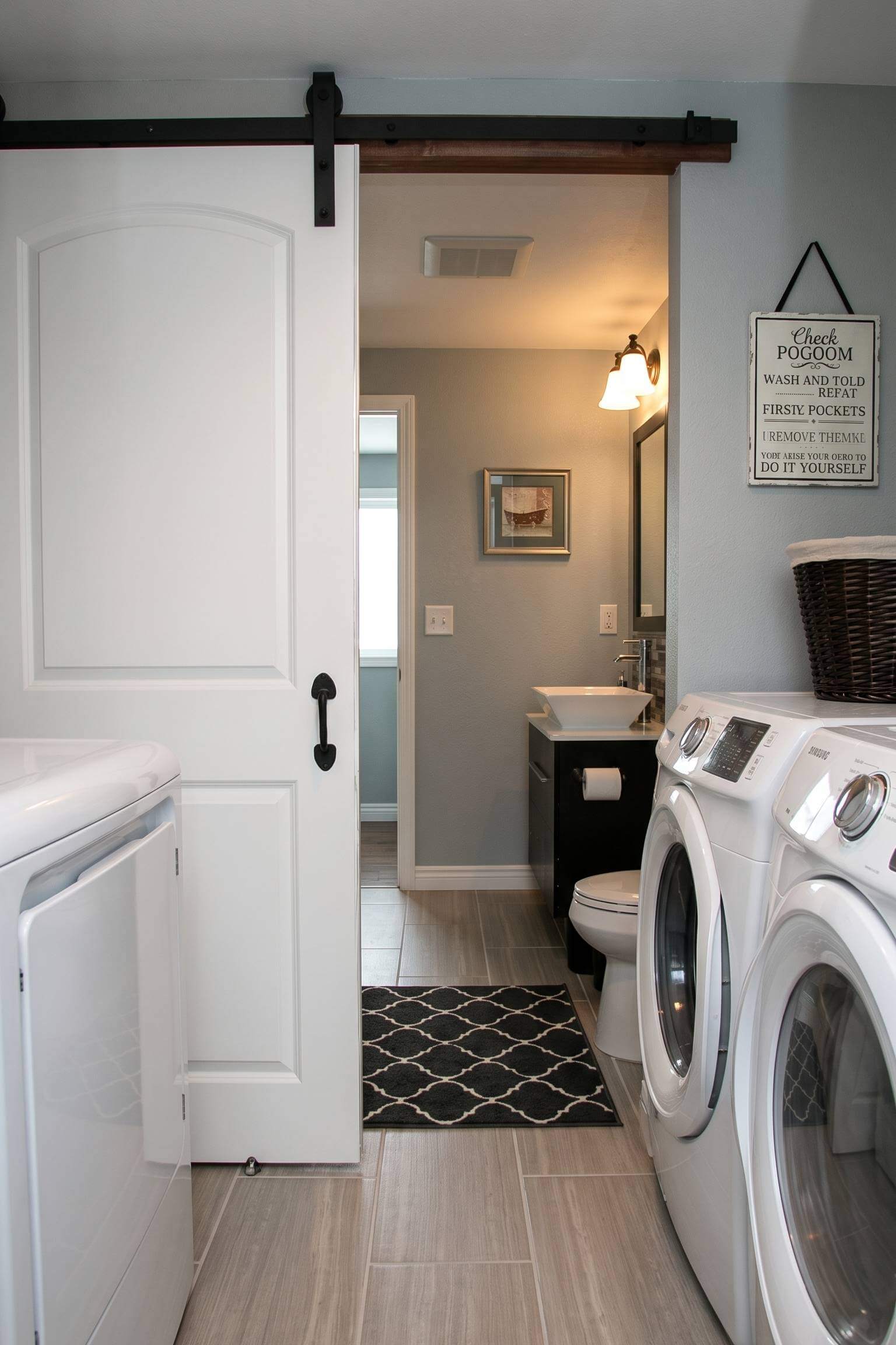 A modern farmhouse bathroom featuring a white sliding barn door that conceals a stacked washer and dryer setup.