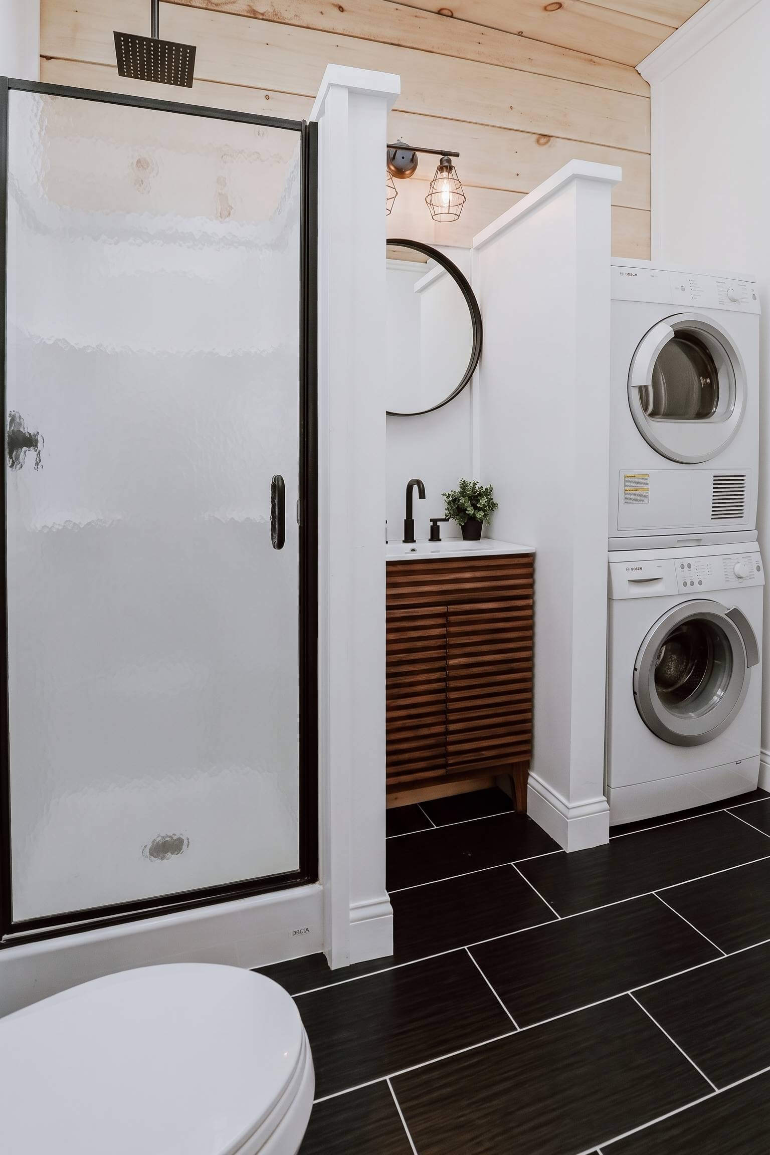 A mid-century modern bathroom featuring a slatted wood vanity next to a stacked washer and dryer.