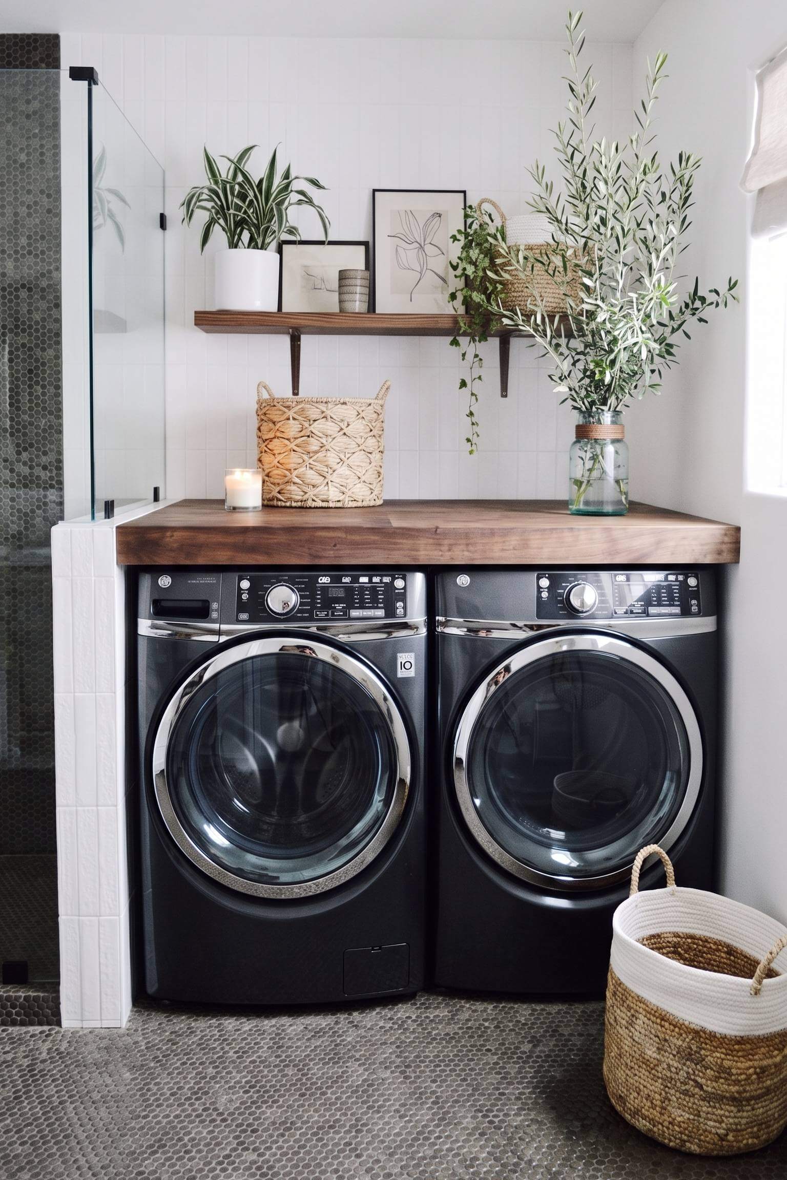 Black front-loading laundry machines under a warm walnut butcher block counter with open wooden shelving above