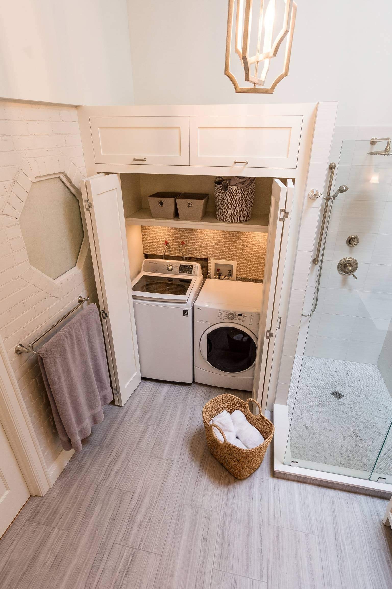 White laundry machines nestled into a quirky painted brick alcove featuring a unique hexagon window.