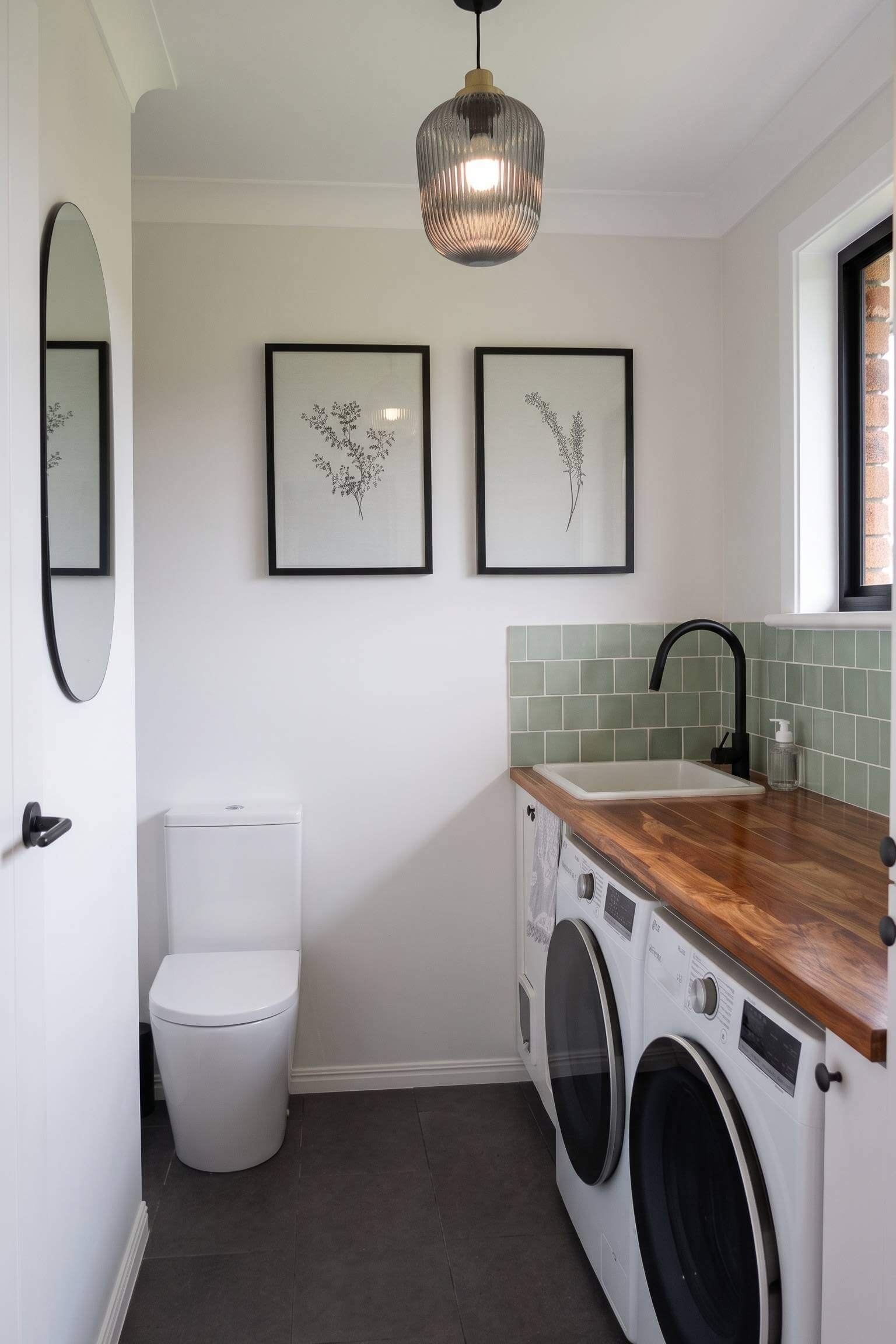 A modern space saving layout featuring front-loading laundry machines tucked under a wood countertop with sage green subway tile.