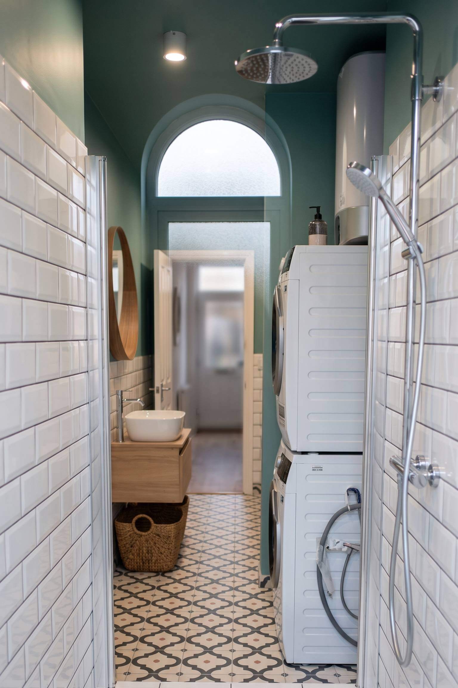 A quirky teal bathroom featuring patterned floor tiles, an arched doorway, and a stacked white washer and dryer