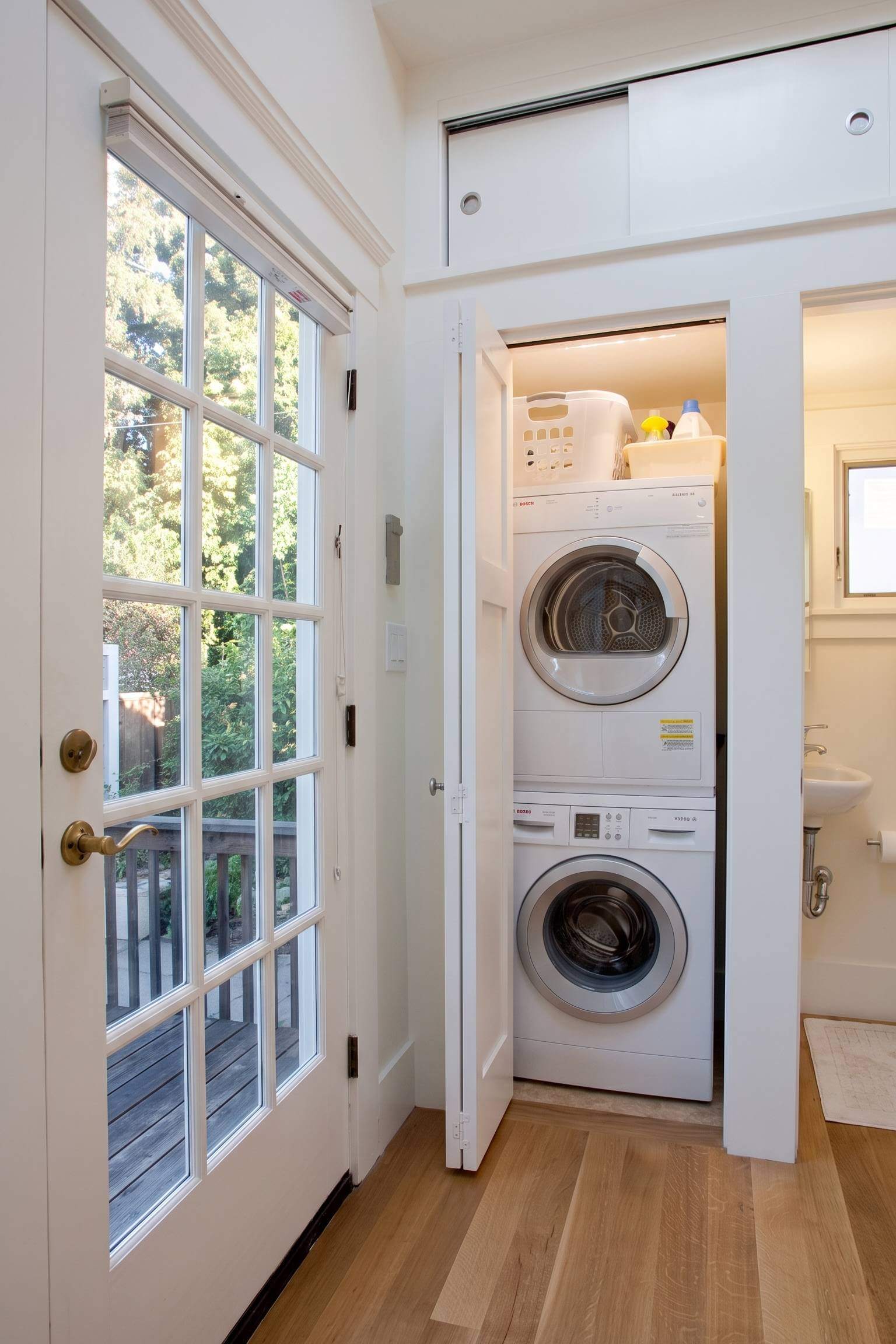 A stacked washer and dryer cleverly hidden behind sleek white sliding doors in a bright modern bathroom
